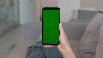 A woman makes a swipe right gesture on a green smartphone screen while lying on the sofa at home. video