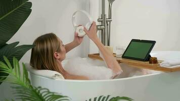 A woman uses a digital device to listen to music while lying in the bathtub. Clicking on the display. video