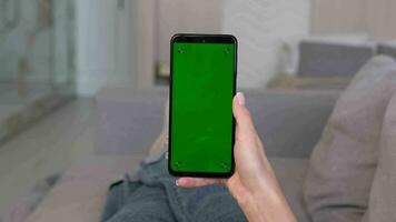 A woman makes a swipe left gesture on a green smartphone screen while lying on the sofa at home. video