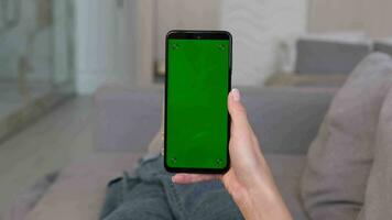 Woman makes swipe up gesture on green screen of smartphone while lying on sofa at home. video