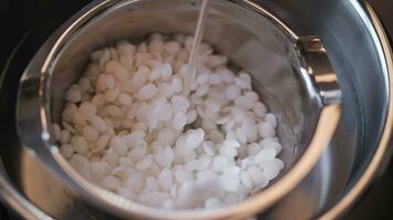 Soy wax flakes are stirred in a container to melt video