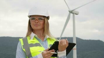 Green alternative in energy a female engineer examines a windmill farm. Development of ecological energy tablet and wind in the hands of scientists. Woman in protective vest analyzing wind power video