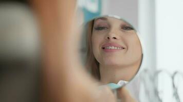 ein Frau sieht aus beim ihr Lächeln im das Spiegel und freut sich im gesund und schön Zähne. das Patienten Lächeln wurden sogar Mehr attraktiv nach Behandlung durch ein Zahnarzt im ein Dental Klinik. Nahaufnahme. video