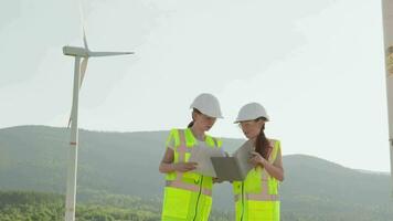 algemeen plan mensen staan tegen achtergrond windmolen elektrisch generator. medewerkers ingenieurs in speciaal kleren helmen vesten gedrag technisch inspectie, beoordelen technisch staat wind macht fabriek video