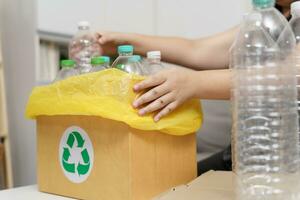 Home recycle eco green zero concept Woman throwing empty plastic bottle in recycling bin with yellow garbage bags at home. photo