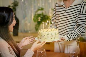 Cheerful friends enjoying home Birthday holiday party. Asian sister cheering drinking red wine celebrating with Birthday cake. photo