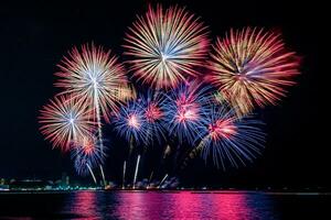 Increíble y hermoso colorido espectáculo de fuegos artificiales en la noche de celebración, que se muestra en la playa del mar con reflejos multicolores sobre el agua foto