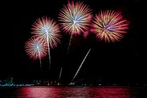 Increíble y hermoso colorido espectáculo de fuegos artificiales en la noche de celebración, que se muestra en la playa del mar con reflejos multicolores sobre el agua foto