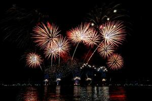 Increíble y hermoso colorido espectáculo de fuegos artificiales en la noche de celebración, que se muestra en la playa del mar con reflejos multicolores sobre el agua foto