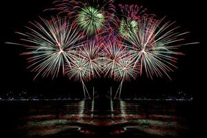 Increíble y hermoso colorido espectáculo de fuegos artificiales en la noche de celebración, que se muestra en la playa del mar con reflejos multicolores sobre el agua foto