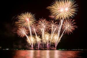 Increíble y hermoso colorido espectáculo de fuegos artificiales en la noche de celebración, que se muestra en la playa del mar con reflejos multicolores sobre el agua foto