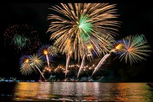 Increíble y hermoso colorido espectáculo de fuegos artificiales en la noche de celebración, que se muestra en la playa del mar con reflejos multicolores sobre el agua foto