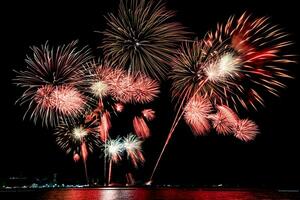 Increíble y hermoso colorido espectáculo de fuegos artificiales en la noche de celebración, que se muestra en la playa del mar con reflejos multicolores sobre el agua foto