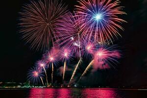 Increíble y hermoso colorido espectáculo de fuegos artificiales en la noche de celebración, que se muestra en la playa del mar con reflejos multicolores sobre el agua foto