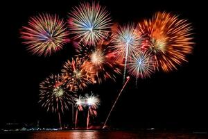 Increíble y hermoso colorido espectáculo de fuegos artificiales en la noche de celebración, que se muestra en la playa del mar con reflejos multicolores sobre el agua foto