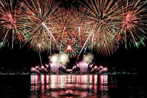 Increíble y hermoso colorido espectáculo de fuegos artificiales en la noche de celebración, que se muestra en la playa del mar con reflejos multicolores sobre el agua foto