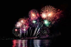 Increíble y hermoso colorido espectáculo de fuegos artificiales en la noche de celebración, que se muestra en la playa del mar con reflejos multicolores sobre el agua foto