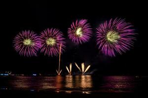 Increíble y hermoso colorido espectáculo de fuegos artificiales en la noche de celebración, que se muestra en la playa del mar con reflejos multicolores sobre el agua foto