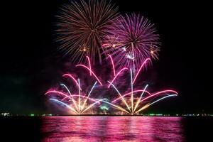 Increíble y hermoso colorido espectáculo de fuegos artificiales en la noche de celebración, que se muestra en la playa del mar con reflejos multicolores sobre el agua foto