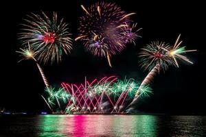 Increíble y hermoso colorido espectáculo de fuegos artificiales en la noche de celebración, que se muestra en la playa del mar con reflejos multicolores sobre el agua foto