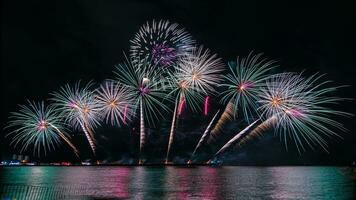 Increíble y hermoso colorido espectáculo de fuegos artificiales en la noche de celebración, que se muestra en la playa del mar con reflejos multicolores sobre el agua foto