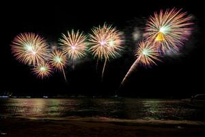 Increíble y hermoso colorido espectáculo de fuegos artificiales en la noche de celebración, que se muestra en la playa del mar con reflejos multicolores sobre el agua foto