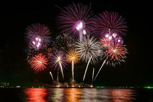 Increíble y hermoso colorido espectáculo de fuegos artificiales en la noche de celebración, que se muestra en la playa del mar con reflejos multicolores sobre el agua foto