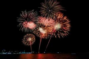 Increíble y hermoso colorido espectáculo de fuegos artificiales en la noche de celebración, que se muestra en la playa del mar con reflejos multicolores sobre el agua foto