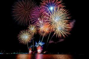 Increíble y hermoso colorido espectáculo de fuegos artificiales en la noche de celebración, que se muestra en la playa del mar con reflejos multicolores sobre el agua foto