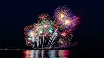 Increíble y hermoso colorido espectáculo de fuegos artificiales en la noche de celebración, que se muestra en la playa del mar con reflejos multicolores sobre el agua foto