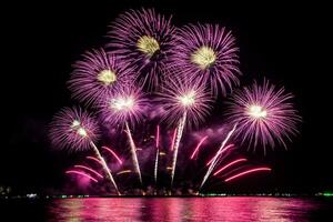 Increíble y hermoso colorido espectáculo de fuegos artificiales en la noche de celebración, que se muestra en la playa del mar con reflejos multicolores sobre el agua foto