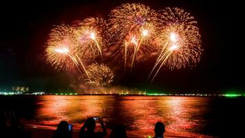 Increíble y hermoso colorido espectáculo de fuegos artificiales en la noche de celebración, que se muestra en la playa del mar con reflejos multicolores sobre el agua foto