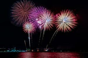 Increíble y hermoso colorido espectáculo de fuegos artificiales en la noche de celebración, que se muestra en la playa del mar con reflejos multicolores sobre el agua foto