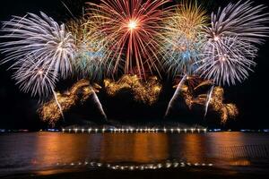 Increíble y hermoso colorido espectáculo de fuegos artificiales en la noche de celebración, que se muestra en la playa del mar con reflejos multicolores sobre el agua foto