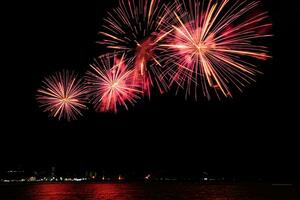 Increíble y hermoso colorido espectáculo de fuegos artificiales en la noche de celebración, que se muestra en la playa del mar con reflejos multicolores sobre el agua foto