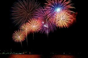 Increíble y hermoso colorido espectáculo de fuegos artificiales en la noche de celebración, que se muestra en la playa del mar con reflejos multicolores sobre el agua foto