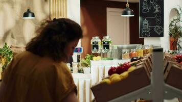 Vegan woman in eco friendly zero waste supermarket adding healthy fruits to shopping basket. Green living client in local neighborhood grocery shop picking farm grown food video