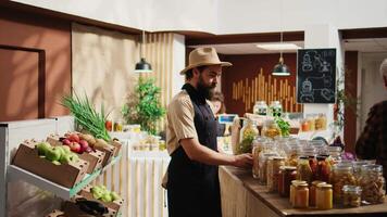 sorridente fornecedor adicionando despensa grampos em eco amigáveis zero desperdício supermercado prateleiras. feliz lojista reabastecimento local Vizinhança mercearia loja com orgânico Comida dentro reutilizável frascos video