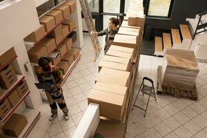 Top view of diverse coworkers working in warehouse, preparing customers orders before start shipping merchandise. Storage room employees in protective overall working with cardboard boxes photo