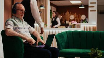 Retired person watches film on laptop using online streaming services, passing time while he is waiting to see accommodation. Old traveller enjoys movie on personal computer in lobby. video