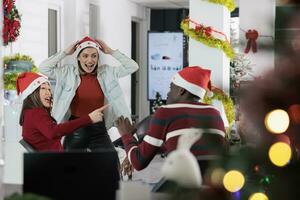 Coworkers having fun in festive decorated office, making fun of each other at work during winter holiday season. Employees laughing together in Christmas ornate workspace photo