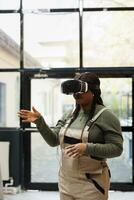 Supervisor checking clients online orders using virtual reality headset before start preparing packages in storage room. African american manager wearing industrial overall during goods inventory photo