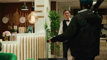 Hotel staff greeting tourist in lobby, bellboy taking trolley bags from guest to ensure pleasant stay upon arrival at wintertime ski resort. Person eager to go skiing on slopes. Handheld shot. video