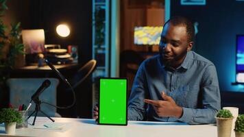 Content creator films chroma key tablet video review for tech enthusiasts. Viral online star hosts technology internet show, unboxing green screen digital device, focus on product