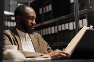 African american prosecutor preparing for case, studying crime matter files in police office. Cop reading forensic expertise report and analyzing investigation clues at night time photo