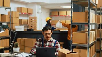 Asian worker showing warehouse supplies to owner, people working on products quality control in storage room. Team of employees looking at merchandise in boxes, business plan. photo