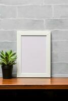 Empty vertical picture frame mockup hanging on a brick wall with wooden desk table and flower vase AI Generated photo