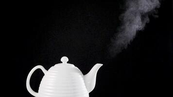 Tea pot on black background with boiling water inside, the steam is rising inthe air. Slow motion footage video