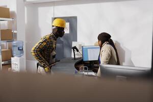 Warehouse manager reading orders list to package handler at counter desk. African american post office employees making invoice for clients parcels at postal storehouse checkout photo