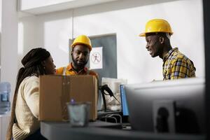 Delivery service employees discussing packages storing at warehouse reception desk. All black postal storehouse men and woman workers team having communication at storage room counter photo